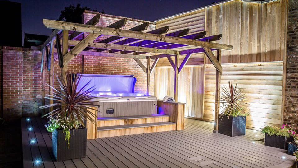 Artesian Island Spas hot tub with a weathered pergola over it and container plants at both front corners of the pergola